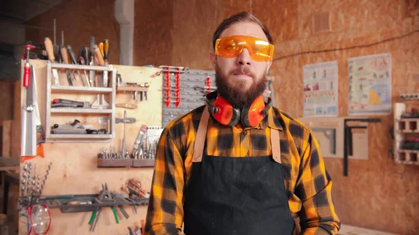 Trabajador barbudo en camisa amarilla y gafas protectoras de pie en el taller —  Fotos de Stock