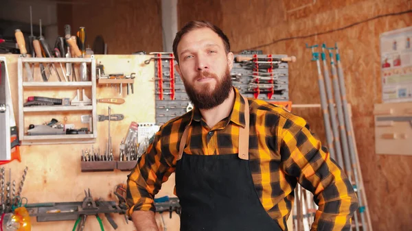 Trabajador barbudo con camisa amarilla de pie en el taller de carpintería - las manos en la cintura —  Fotos de Stock