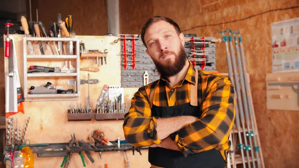 Trabajador barbudo con camisa amarilla de pie en el taller - cruzando las manos —  Fotos de Stock