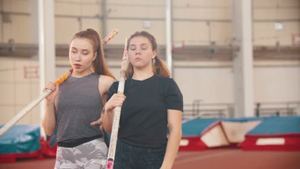 Entrenamiento de bóveda de poste: dos jóvenes deportistas de pie en el estadio sujetando postes y mirando a la cámara — Vídeos de Stock