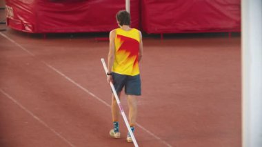 Stadyumdaki sırıkla atlama eğitimi. Pistte direğini tutan atletik bir adam.