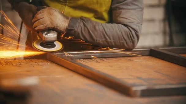 Άνθρωπος εργαζόμενος λείανση τις ραφές ενός σιδερένιου πλαισίου στο εργαστήριο - αστράφτει βγαίνει από το μέταλλο — Αρχείο Βίντεο
