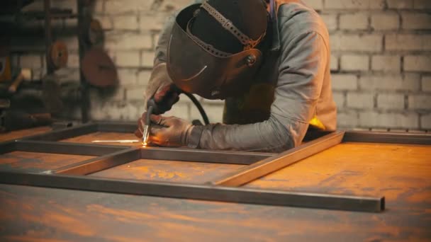 Un hombre con un casco protector soldando las costuras entre las vigas de metal — Vídeos de Stock