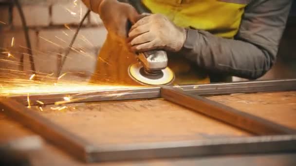 Man worker grinding the seams of an iron frame — Stock Video