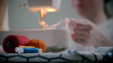 Genç bayan tasarımcı dikiş makinesinin yanında, elbise ve rozetlerle çalışıyor.