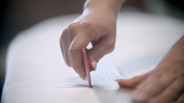 Молода жінка швачка робить позначки за допомогою мила і лінійки на тканині для різання — стокове відео