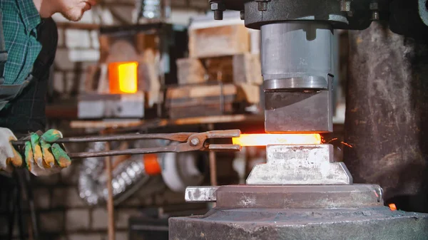 Blacksmith working - putting a longer piece of metal under the pressure of industrial forging machine — Zdjęcie stockowe