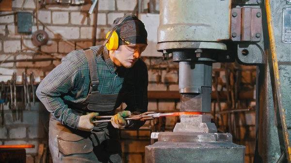 Forging industry - a blacksmith putting the hot piece of metal under the pressure of big machine