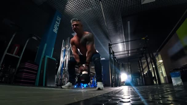 Een man met grijs haar bodybuilder trekt een kettlebell in de sportschool — Stockvideo