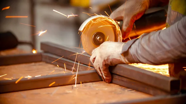 Un operaio uomo taglio trave metallica a metà utilizzando macchina smerigliatrice — Foto Stock
