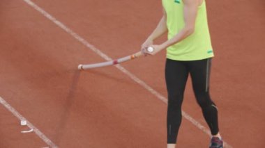 Stadyumdaki sırıkla atlama eğitimi. Atletik bir adam direğini yerden kaldırıyor.