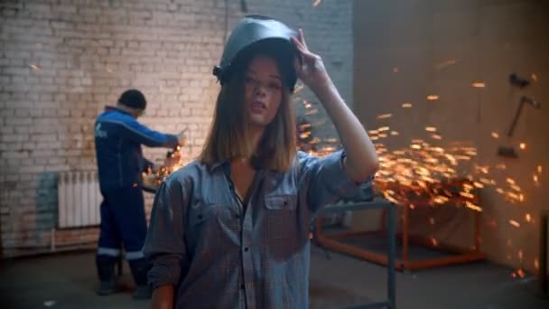 Молодая сексуальная женщина, стоящая в мастерской и надевающая шлем, держа угловую мельницу — стоковое видео