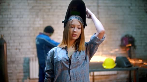 Young sexy smiling woman standing in the workshop in protective mask holding an angle grinder — Stock Video