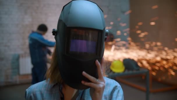 Молодая сексуальная улыбающаяся женщина, стоящая в мастерской, снимая защитную маску — стоковое видео