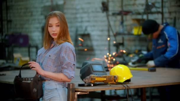 Junge sexy lächelnde Frau steht in der Werkstatt - Mann arbeitet im Hintergrund — Stockvideo