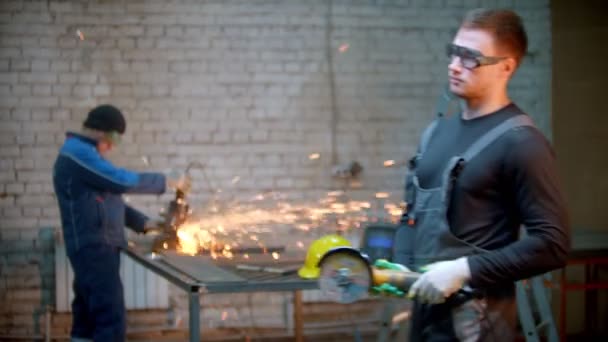 Junger schöner Mann steht in der Werkstatt und hält einen Winkelschleifer — Stockvideo