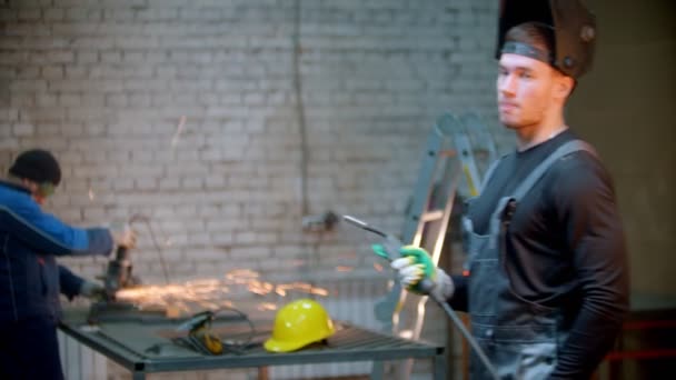 Joven hombre guapo de pie en el taller sosteniendo un instrumento de soldadura — Vídeos de Stock
