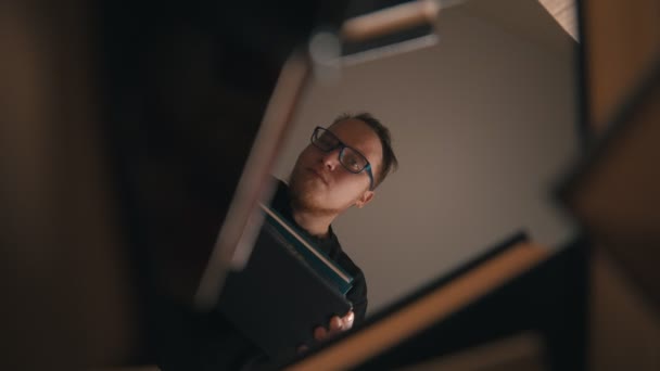 Un joven con gafas mirando en el hueco alrededor de los libros y poniendo el libro en él — Vídeo de stock