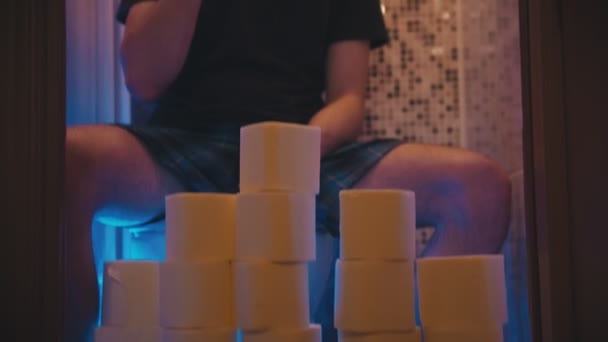Un joven sentado en un inodoro con un montón de papel higiénico — Vídeo de stock