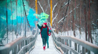 İki genç kadın yeşil ve mavi duman bombalarıyla karlı köprüde koşuyor.