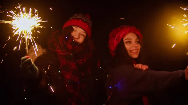 Two young women standing on the snowy bridge holding sparklers at night — Stock Photo, Image