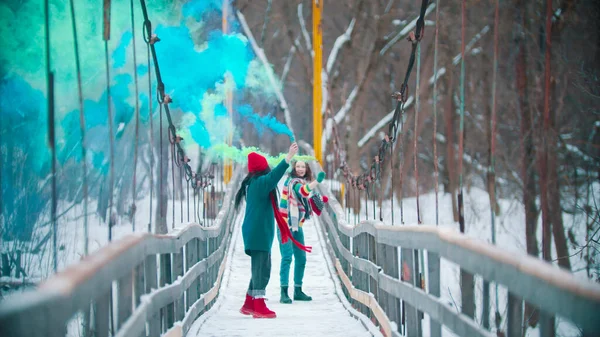 冬の間緑と青の煙の爆弾で楽しんで雪の橋を走っている2人の若い女性 — ストック写真