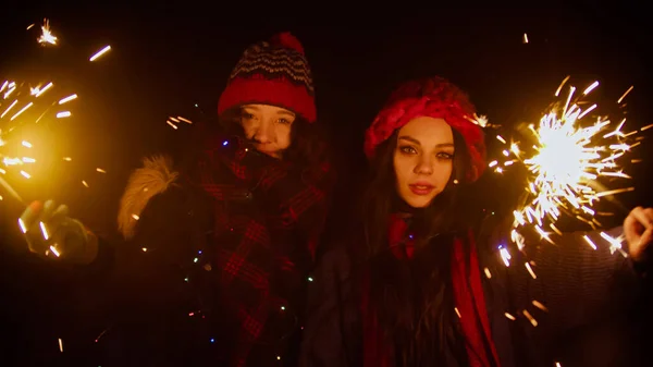 Two young women friends holding sparklers at night while walking — Stock Photo, Image