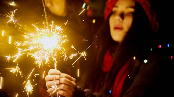 Young pretty woman holding bright sparkler at night outdoors — Stock Photo, Image