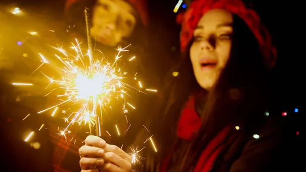 Young women holding sparklers at night and looking at it — Stock Photo, Image