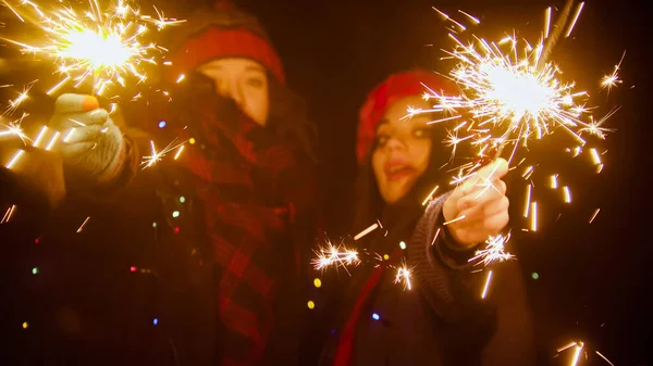 Young women smiling holding sparklers at night — Stock Photo, Image