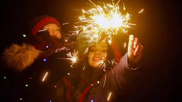 Young smiling women friends holding bright sparklers at night — Stock Photo, Image