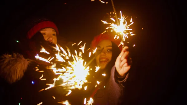 Young smiling women friends holding bright sparklers at night outdoors — Stock Photo, Image