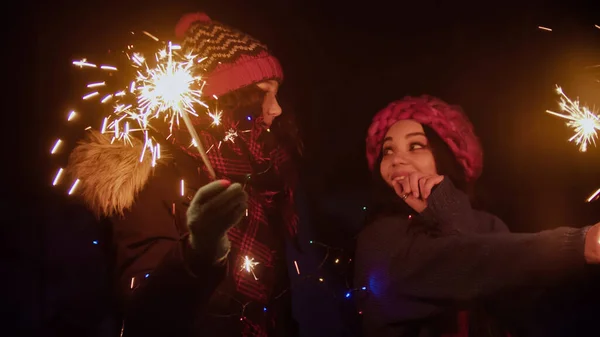 Two young women friends walking outdoors holding bright sparklers — Stock Photo, Image