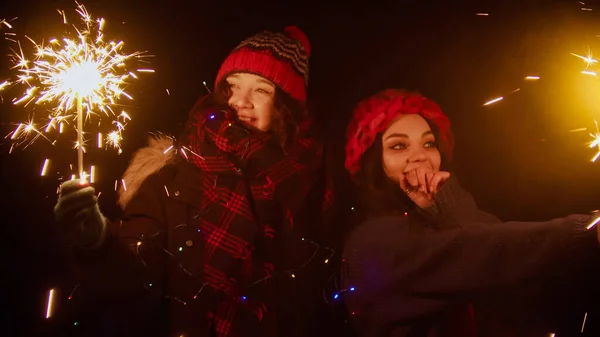 Two young smiling women friends walking outdoors holding bright sparklers — Stock Photo, Image