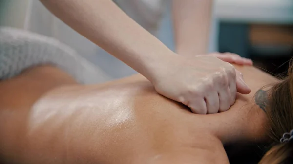 Procedimiento de masaje - masaje maestro masajear a las mujeres de nuevo con el tatuaje usando aceite de masaje — Foto de Stock