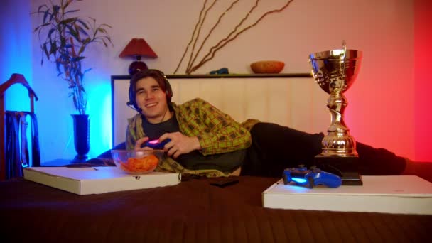 Młody człowiek leży na łóżku i gra w gry wideo — Wideo stockowe