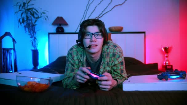 Jongeman in koptelefoon liggend op het bed het spelen van video game online — Stockvideo