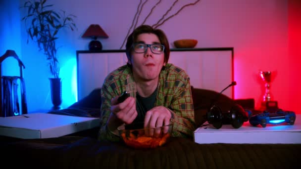 Mladý pohledný muž v brýlích ležící na posteli a dívající se na televizi — Stock video