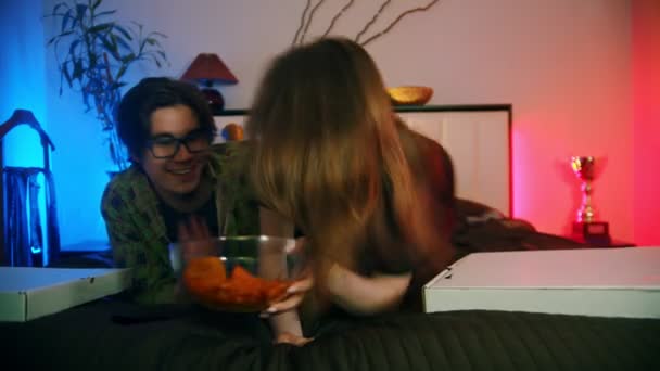 Junge Frau bringt ihrem Freund Chips aufs Bett — Stockvideo