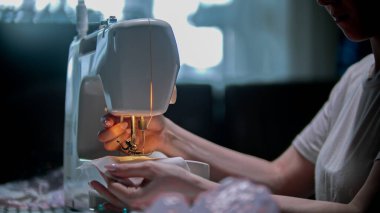 Genç bayan terzi içeride beyaz bir maske dikiyor.