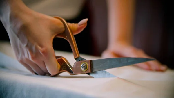 Genç kadın terzi, kumaşı büyük bir makasla kesiyor.
