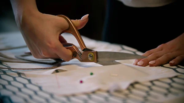 Jovem costureira cortando pano branco com grande tesoura — Fotografia de Stock