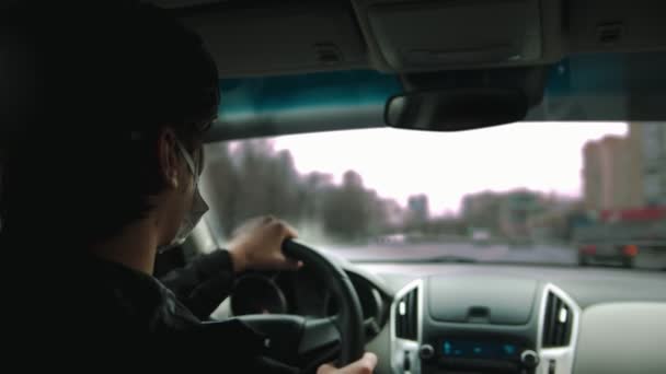Jeune homme en masque de protection conduisant une voiture et regardant par les fenêtres — Video