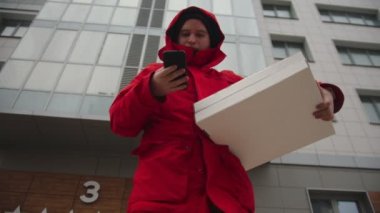 Pizza getiren bir kurye. Etrafa bakıyor ve telefonla konuşuyor.