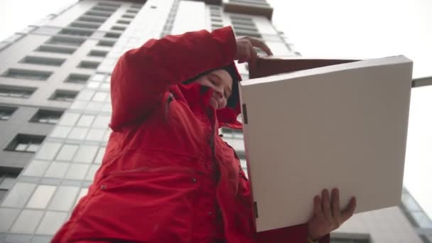 En man kurir levererar pizza - tar en bit och biter den — Stockvideo
