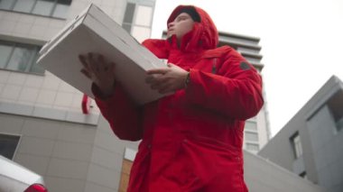 Pizza getiren bir adam. Etrafa bakıyor ve müşteriyi bekliyor.