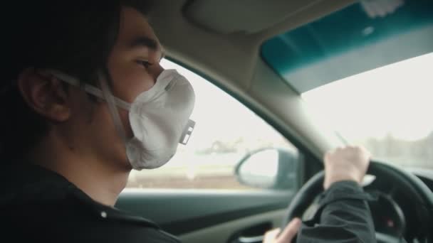 Молодой человек в защитной маске водит машину в плохую погоду — стоковое видео
