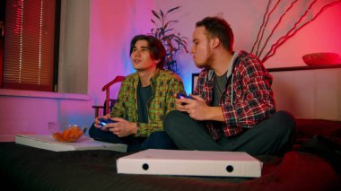 Yatakta oturmuş oyun oynayan iki genç adam.