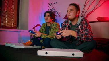 İki genç erkek arkadaş yatakta oturmuş oyun oynuyorlar.