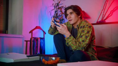 Yatakta oturmuş video oyunu oynayan heyecanlı genç adam.